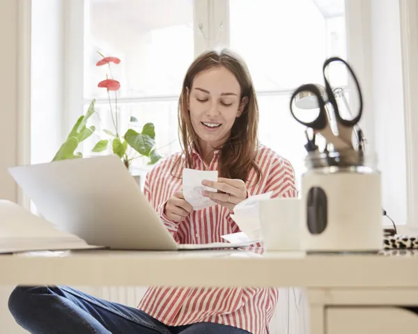 Ung kvinne på hjemmekontor ser på en kvittering foran pcen sin