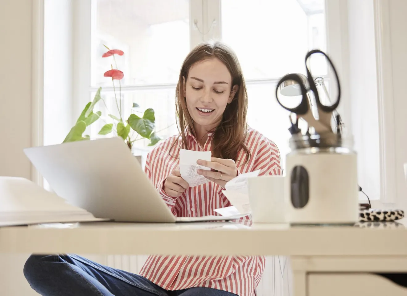 Ung kvinne på hjemmekontor ser på en kvittering foran pcen sin