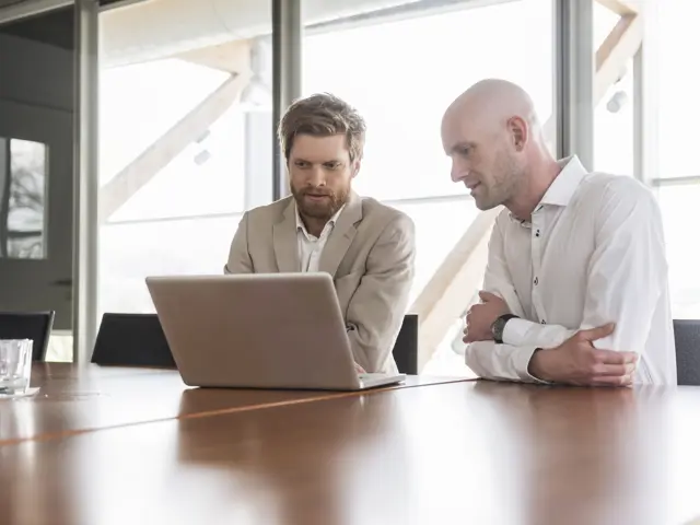 To menn sitter foran en laptop