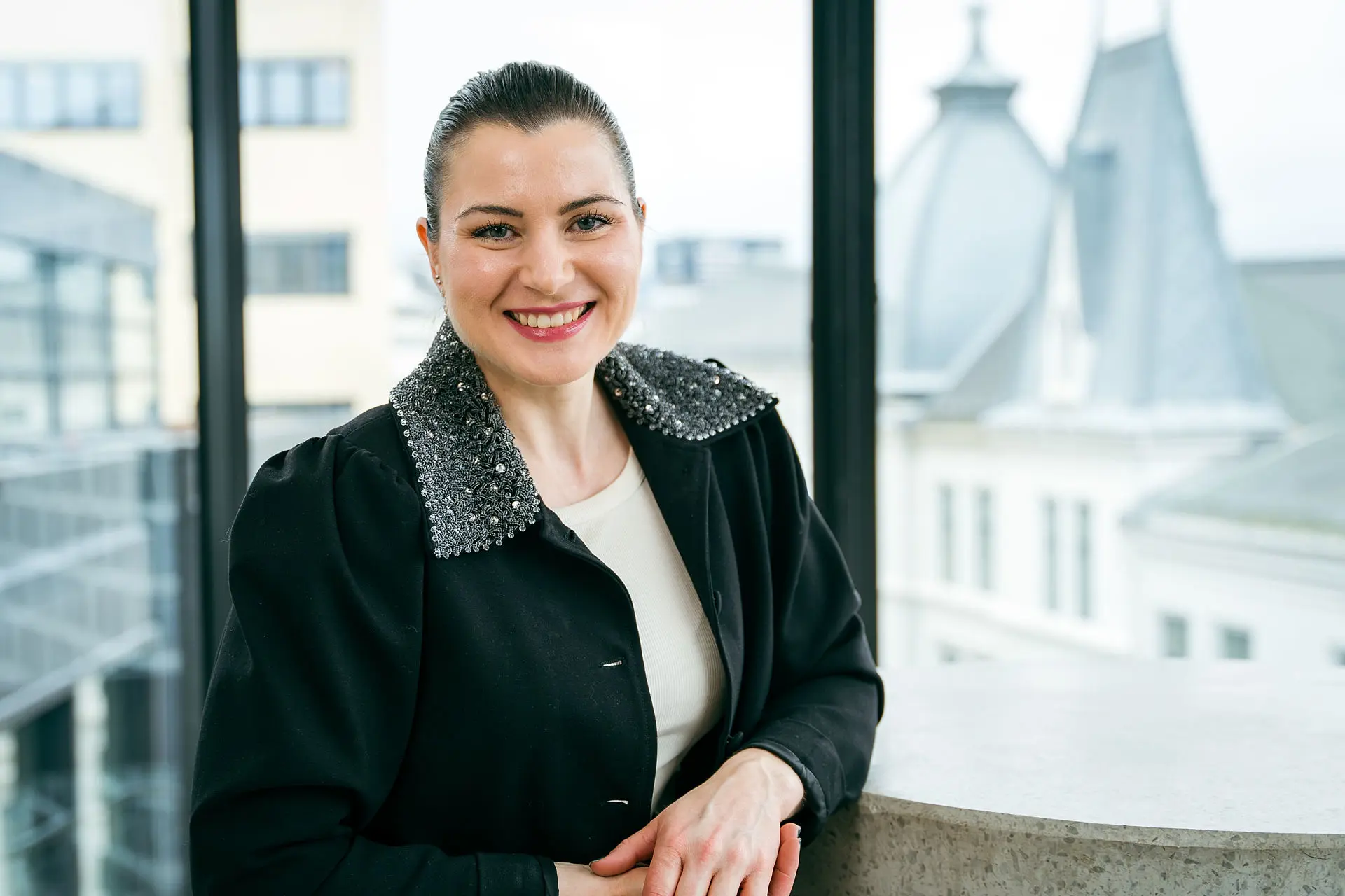 President Elisabet Haugsbø med svart jakke, hvit genser, smiler foran vindu med utsikt over oslo 
