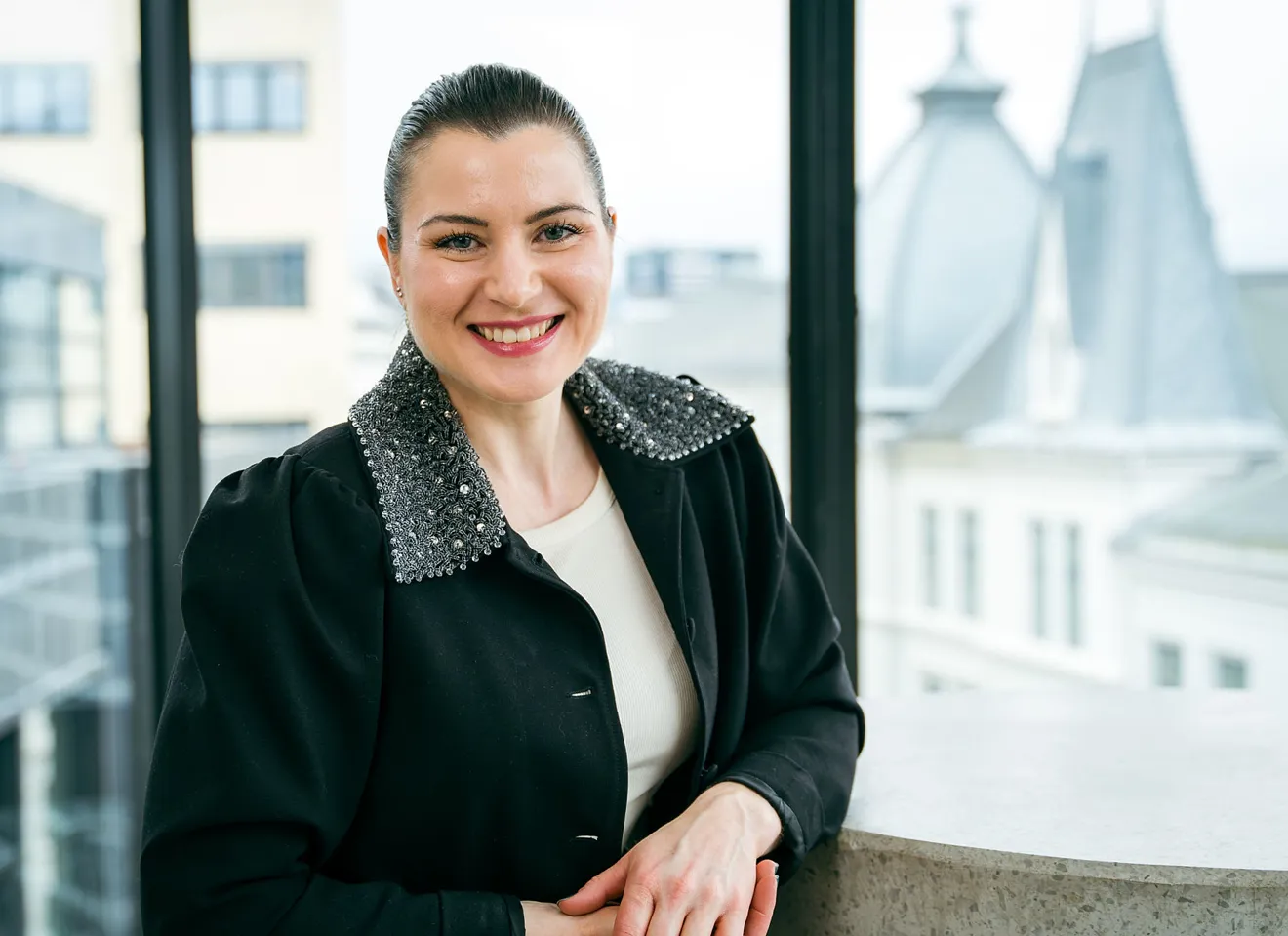 President Elisabet Haugsbø med svart jakke, hvit genser, smiler foran vindu med utsikt over oslo