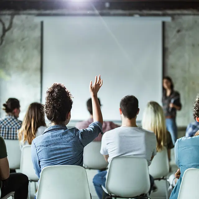 Forsamling mennesker i ett møte der en kvinne rekker opp hånden
