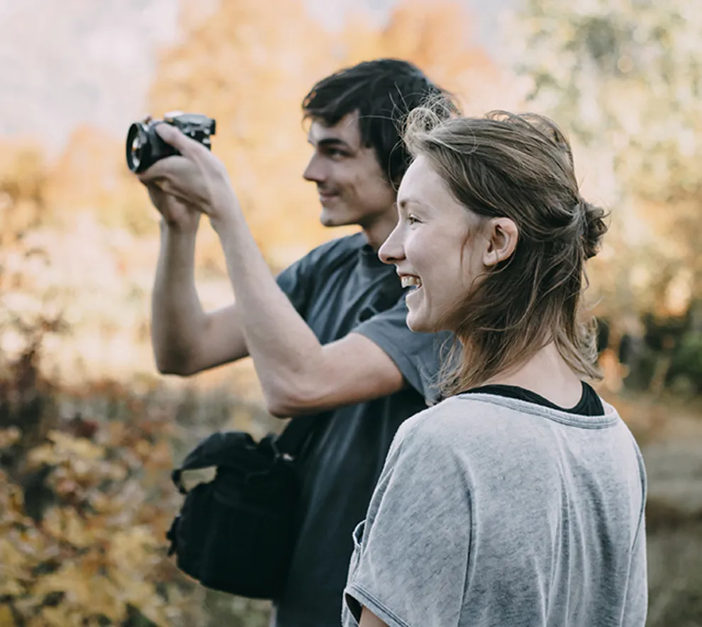 Mann og kvinne i naturen på høsten tar bilder med systemkamera