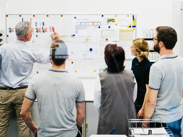 En gruppe medarbeidere står foran et whiteboard og planlegger sammen