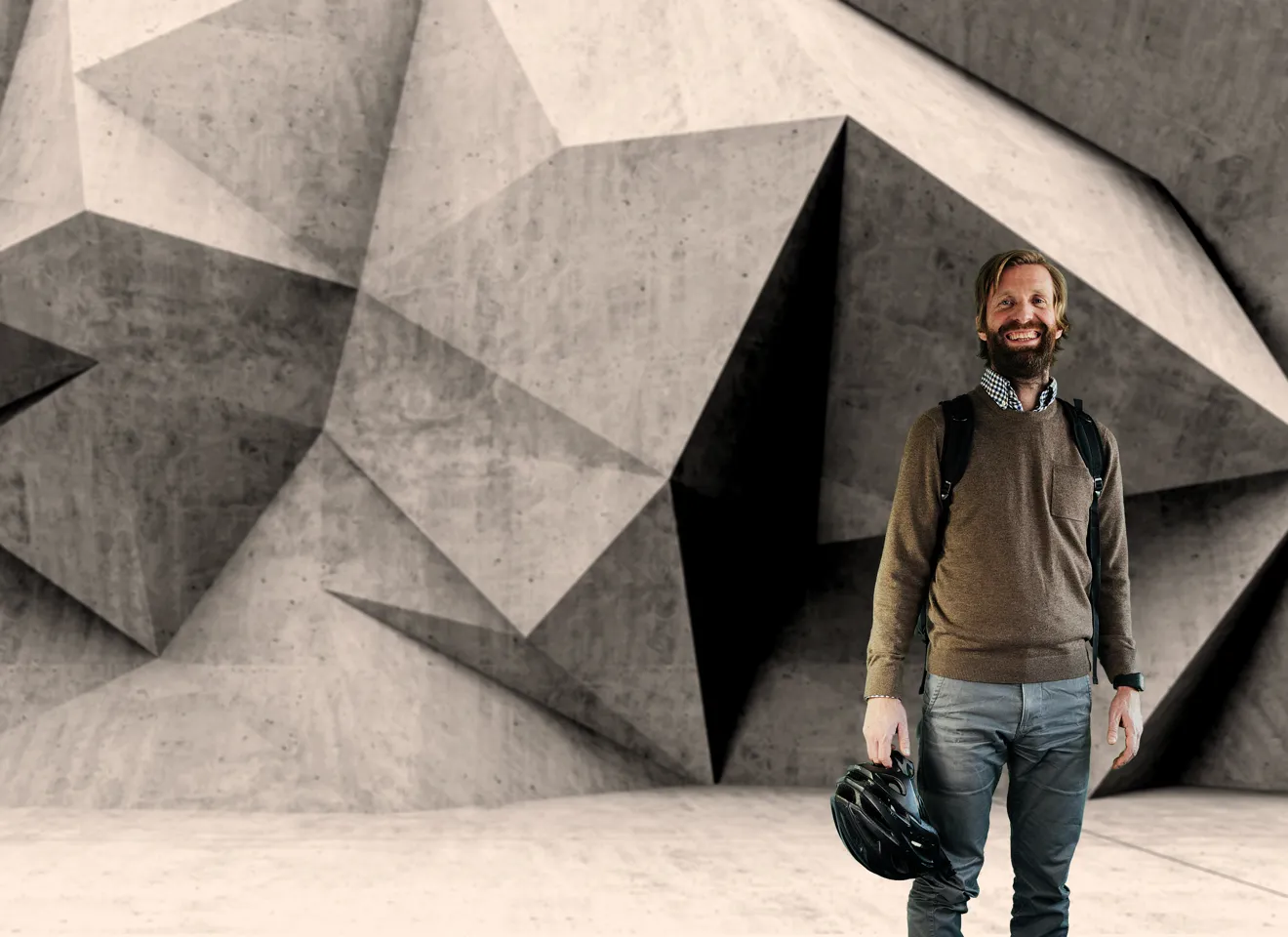 En mann med stor smil stående foran en kunstnerisk betong vegg