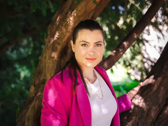 Kvinne står ute, ser inn i kamera.