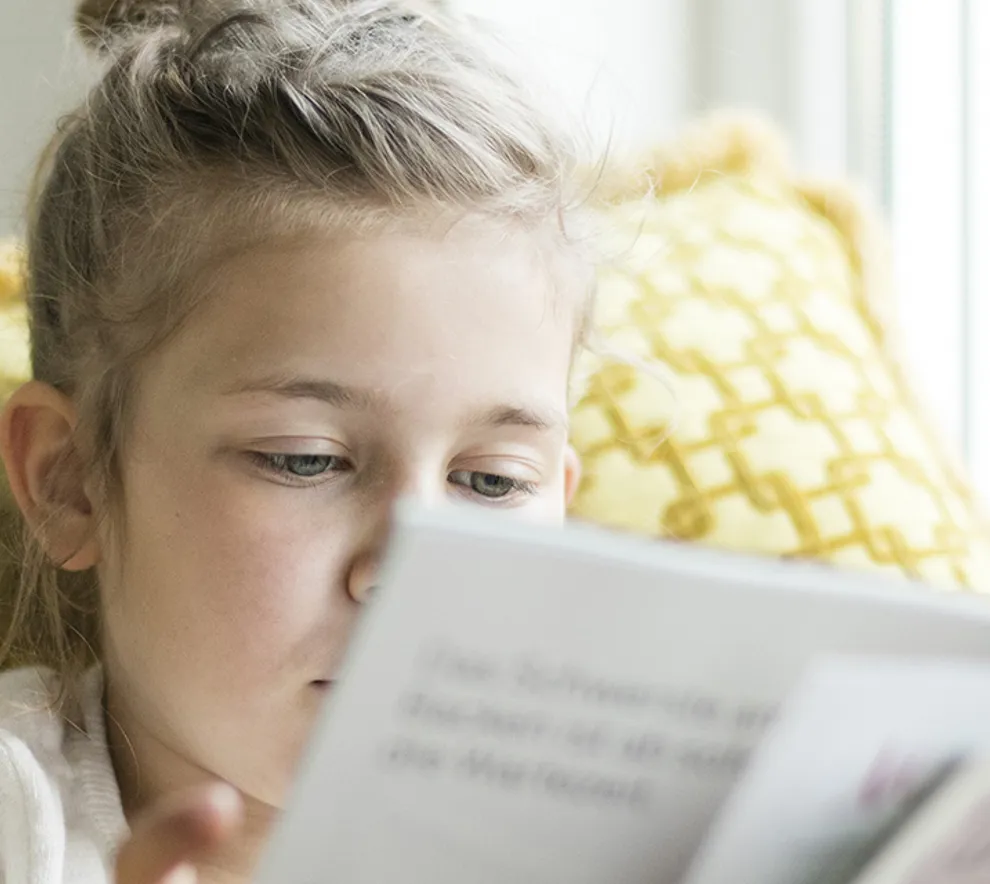 Illustrasjonsbilde av et barn, en jente, som sitter og leser en bok