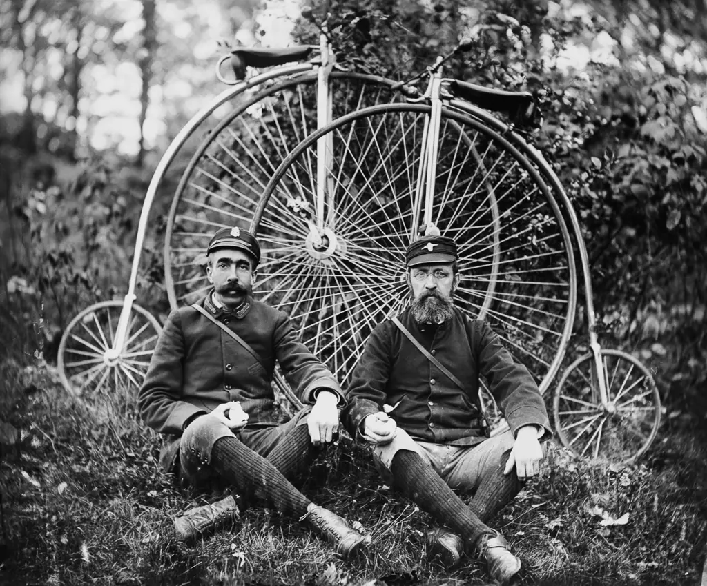 To menn i unifrom sitter foran to gamle bicycler