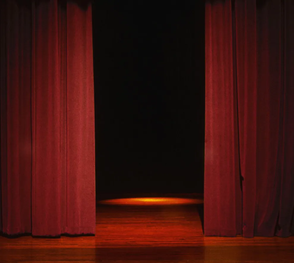 Rødt sceneteppe nesten lukket på mørklagt scene med lokalt lys midt på