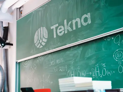 Grønn tavle med formler og Tekna-logo skrevet i kritt
