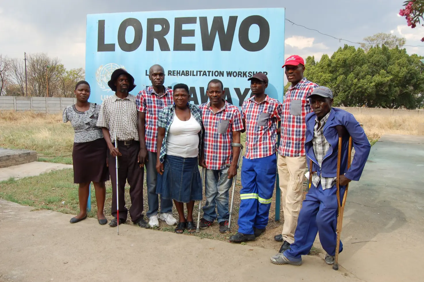 En gruppe afrikanske voksne med handikapp foran et LOREWO skilt