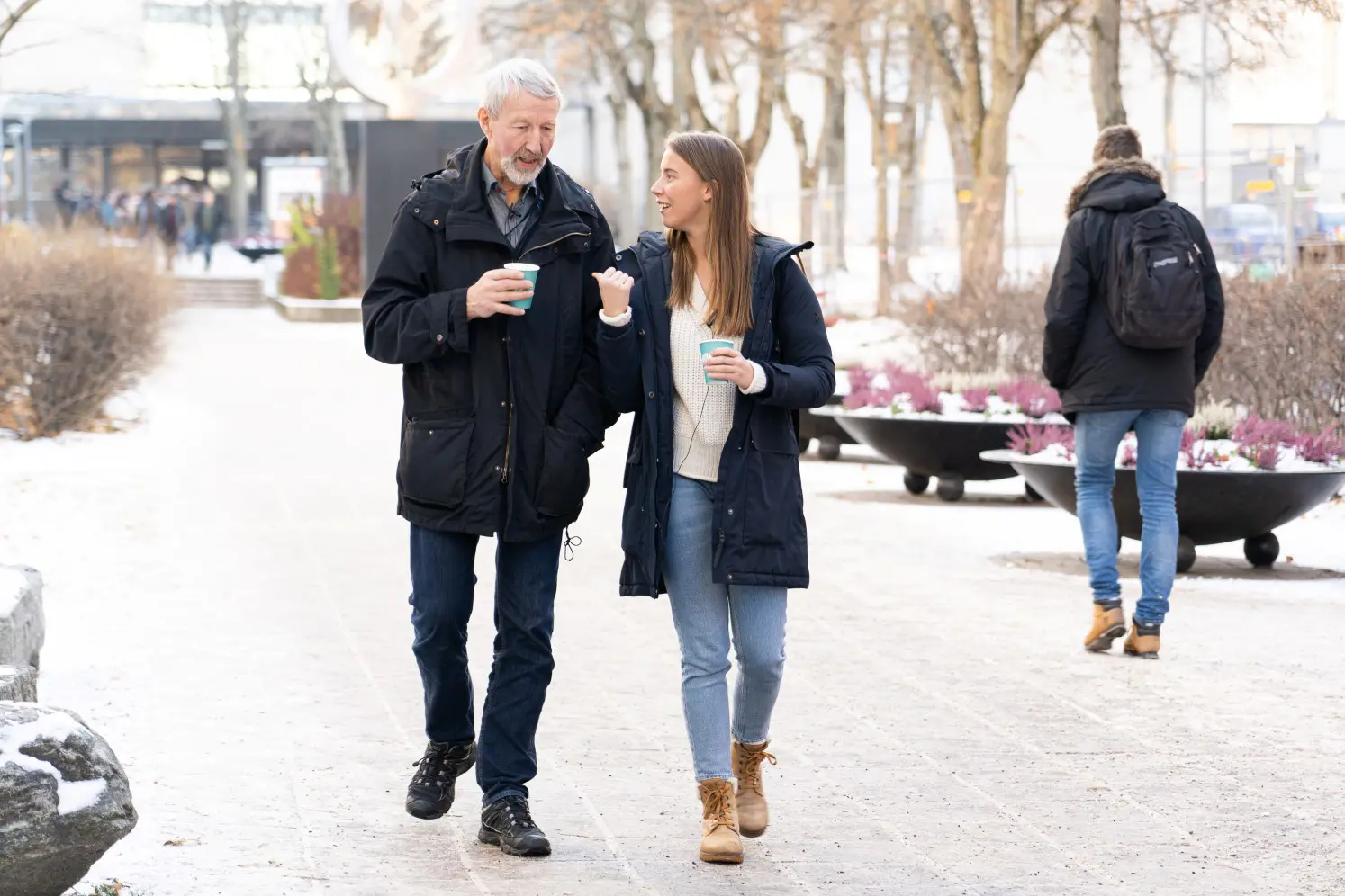 Sanne og Terje i samtale mens de spaserer i en park med en kopp kaffe i hånden