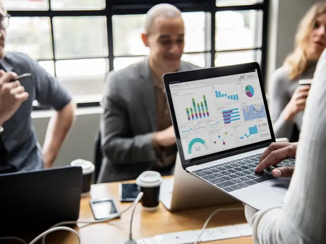 Illustrasjonsbilde av en kvinne som holder en åpen laptop. Tre andre personer er uskarp i bakgrunn, sitter og hører på kvinnen