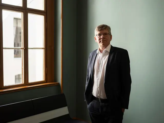 Mann i dress står ved vindu