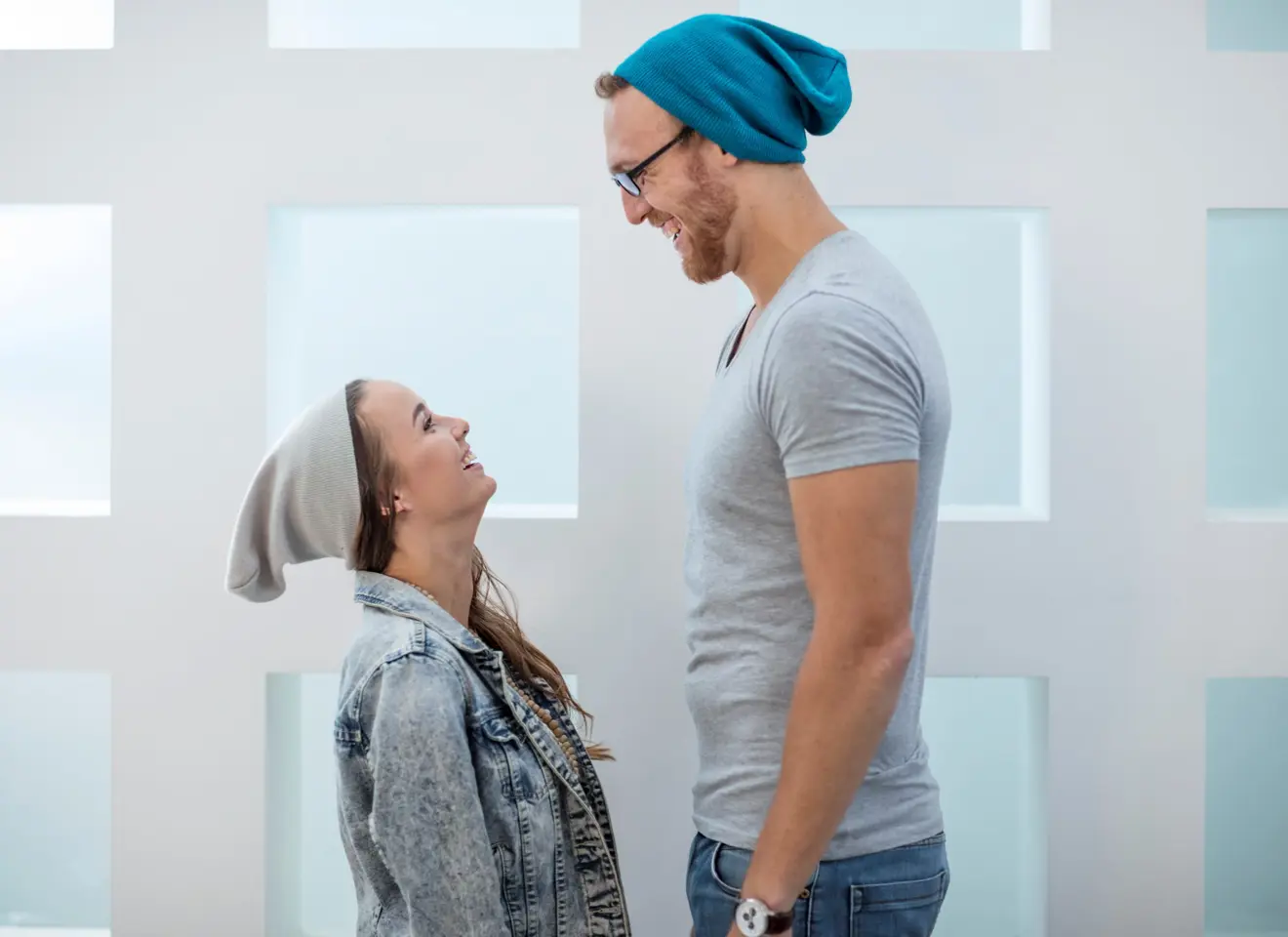 Lite kvinne og stor mann med luer ler mot hverandre