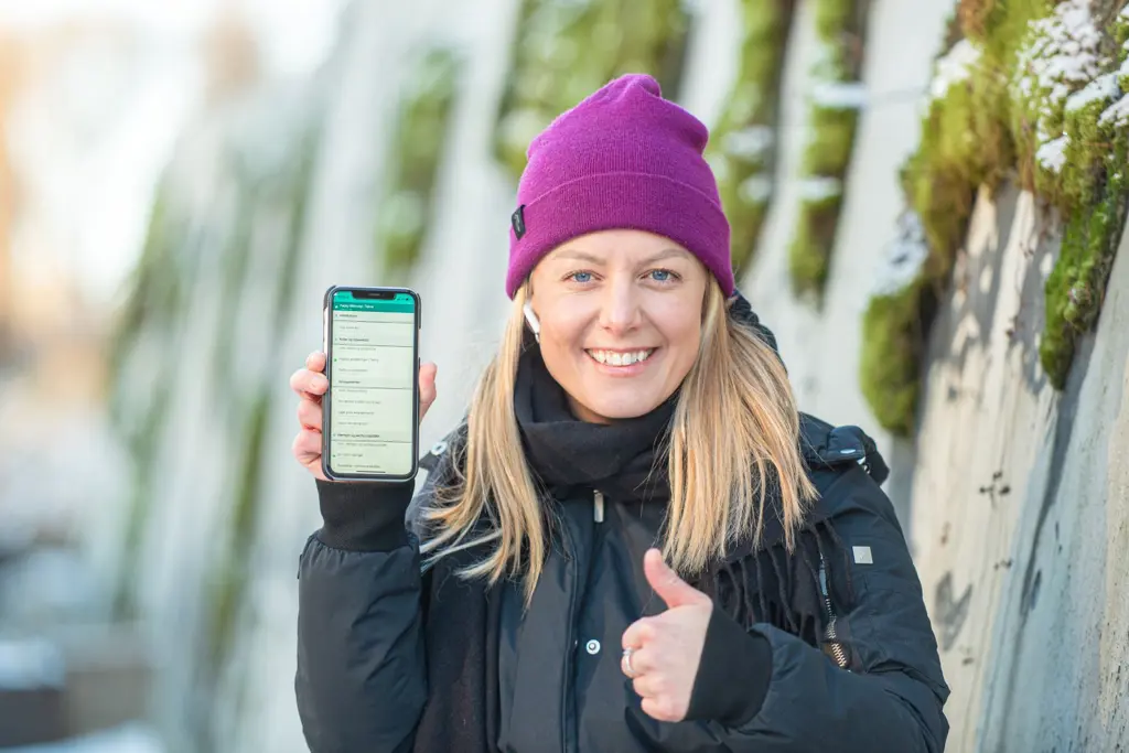 Anne Cathrine Strande Straube holder opp en smarttelefon med e-læringsprogram og viser tommel opp