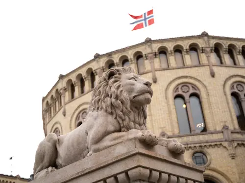 Løven foran Stortinget og flagg som vaier på toppen av bygget
