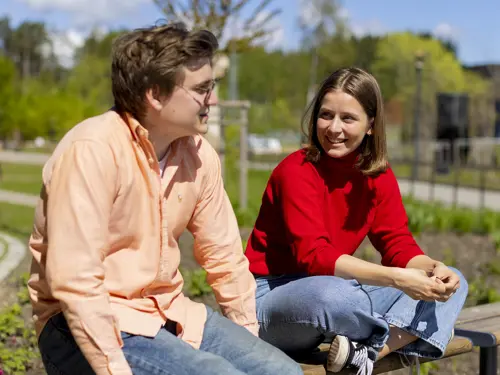 To unge studenter sitter ute i sola på en benk