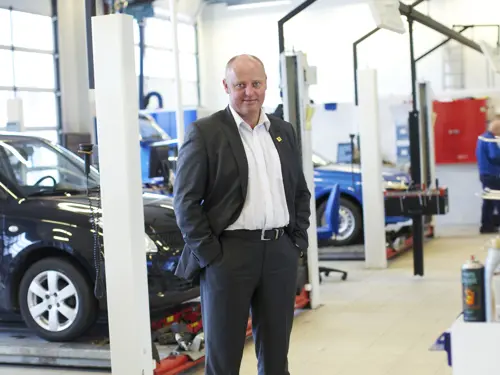 Stig Skjøstad står foran flere biler i et bilverksted