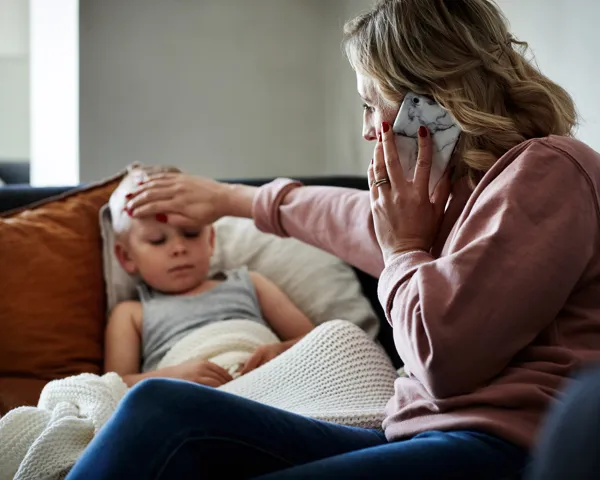 Bekymret kvinne kjenner på en gutts panne mens hun snakker i telefonen