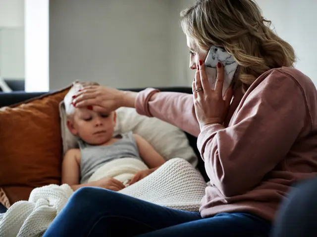 Bekymret kvinne kjenner på en gutts panne mens hun snakker i telefonen