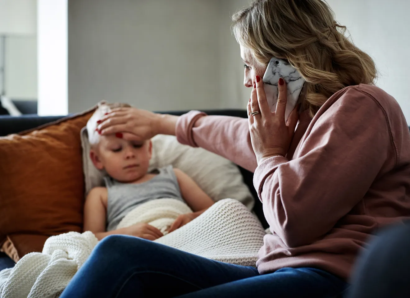 Bekymret kvinne kjenner på en gutts panne mens hun snakker i telefonen
