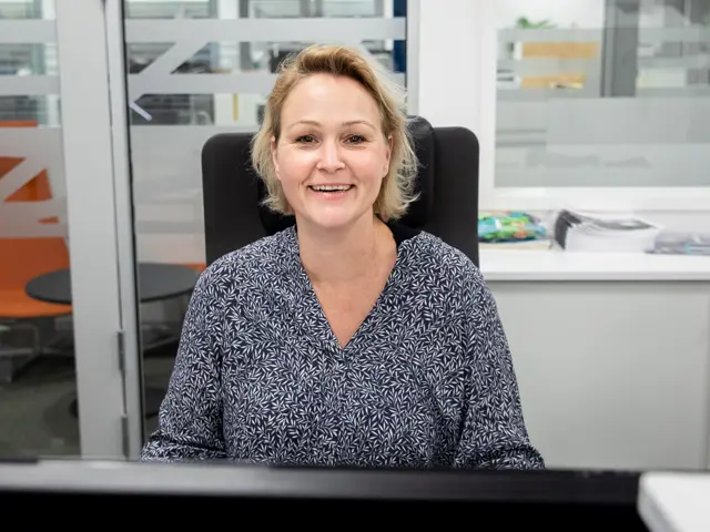 Katrine Olsson sitter på kontoret og smiler til kamera