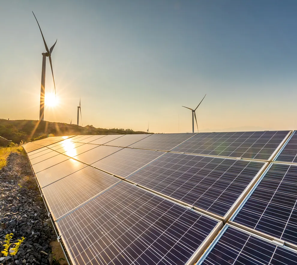 Bilde av to vindmøller og solceller i solnedgang