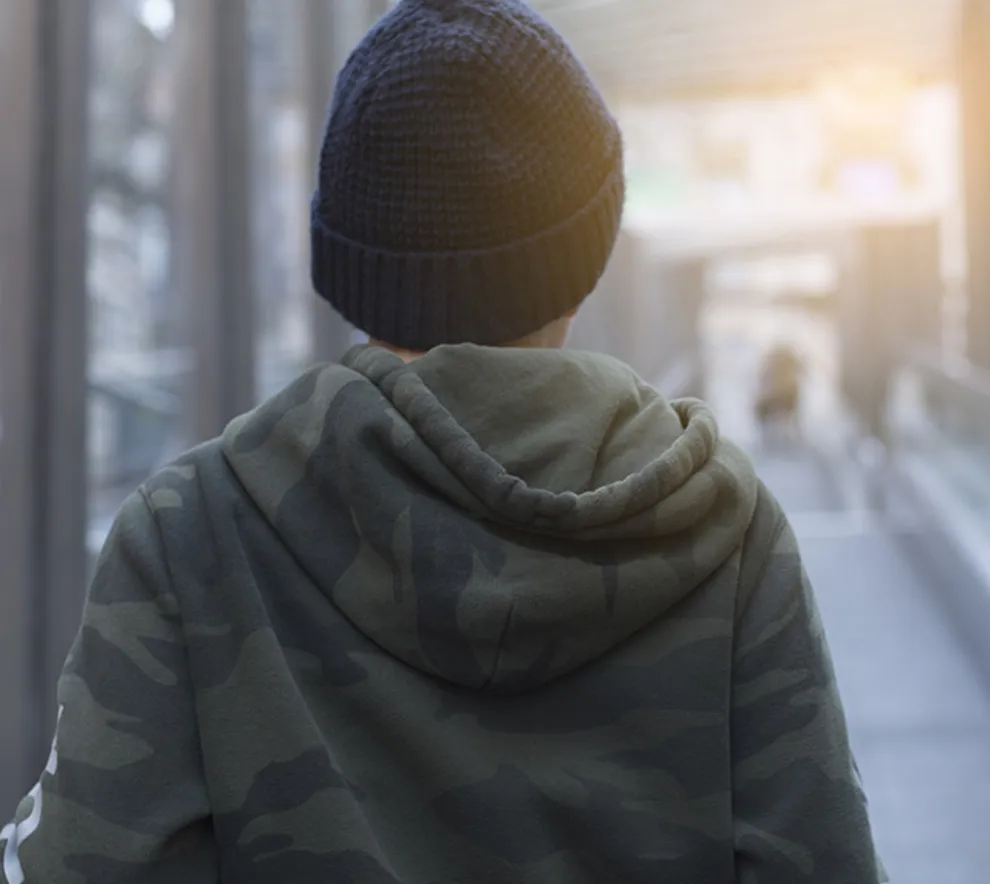 En gutt med hettegenser og lue som går over gangbro