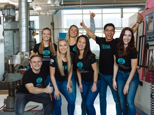 En gruppe glade studenter med Tekna T-skjorter i et teknisk verksted
