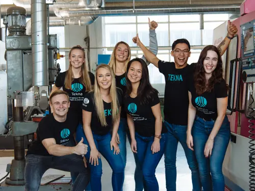 En gruppe glade studenter med Tekna T-skjorter i et teknisk verksted