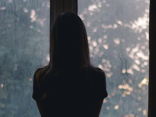 Person sett bakfra stirrer ut et regnfylt vindu