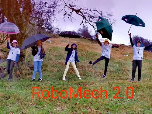 bilde av fem unge personer med paraply i åpent landskap. Digitalt pålagt tekst: RoboMech 2.0 i rød skrift står under personene på gresset. 
