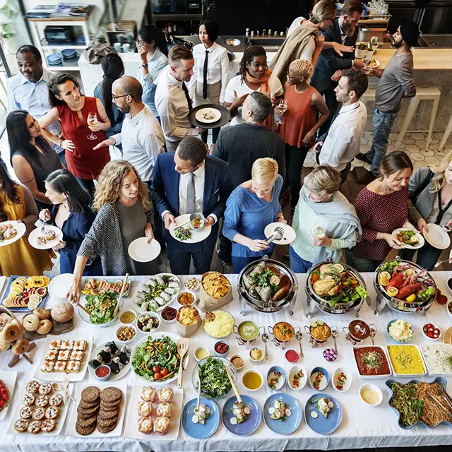 Mange mennesker mingler foran stående buffet