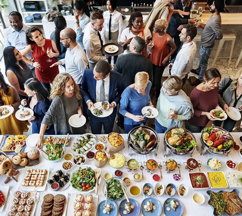 Mange mennesker mingler foran stående buffet