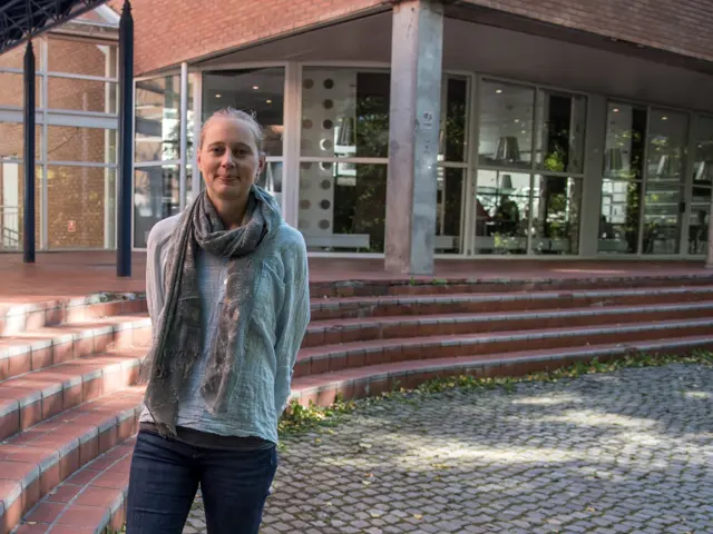 Cecilie står utendørs foran en liten trapp opp til et moderne bygning