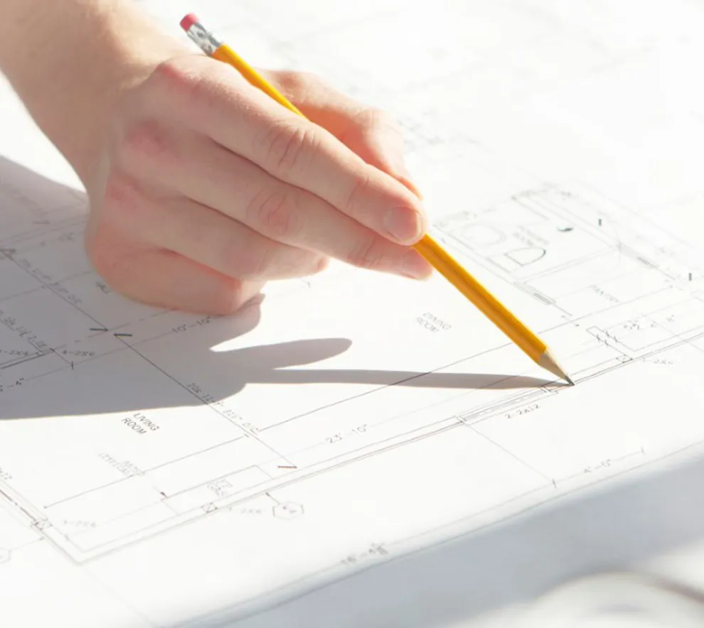 En hånd med en blyant som tegner på en planskisse over en bolig