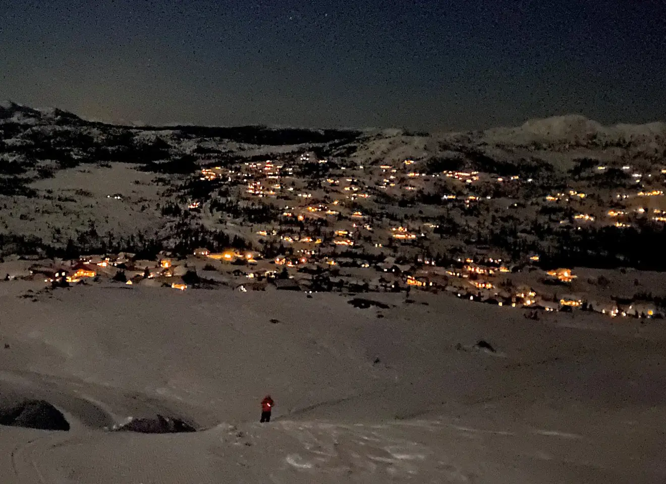 Snødekket fjell med lys fra hytter om natten