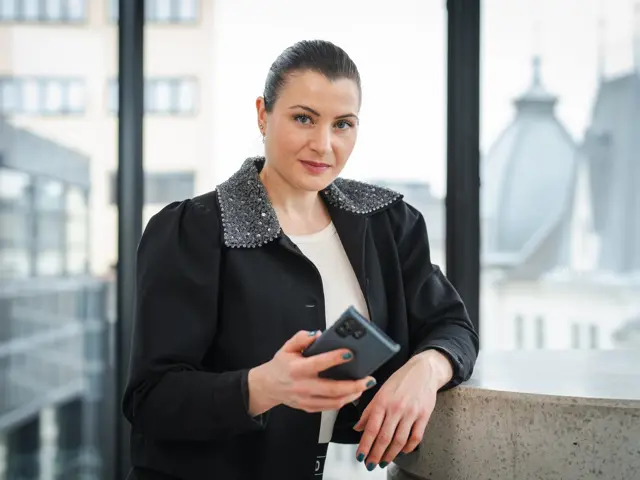 President Elisabet Haugsbø inne i kontorlandskap, med mobil i hånda, svarte klær, alvorlig ansiktsuttrykk