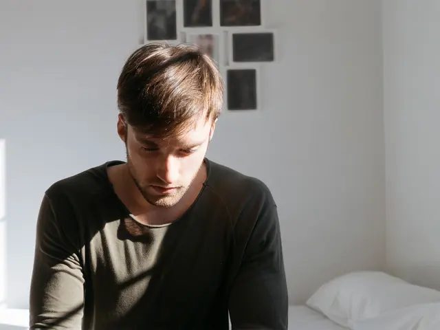 Person sitter på sengekant og stirrer ned i bakken