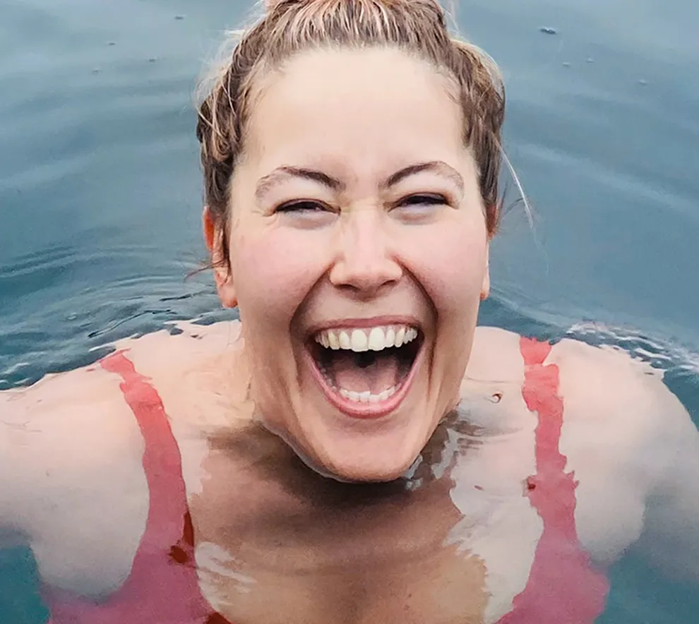 Smilende kvinne bader i havet på vinteren