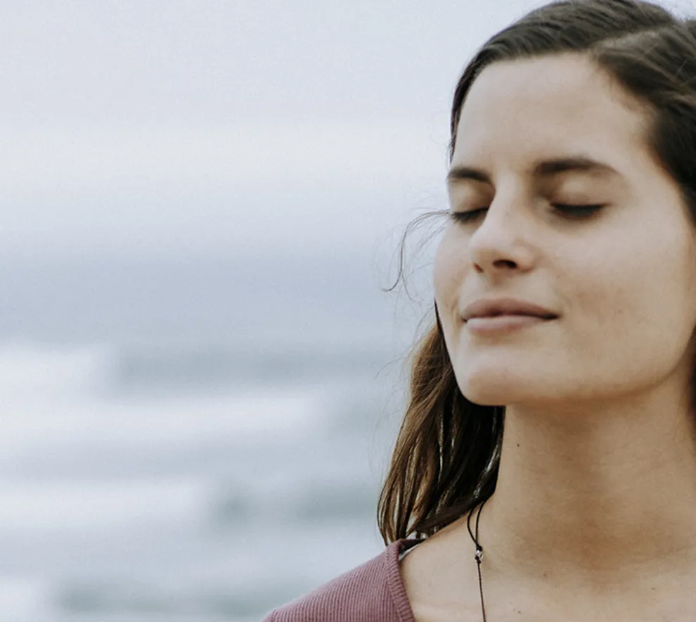 Kvinne ved havet lukker øynene og mediterer.