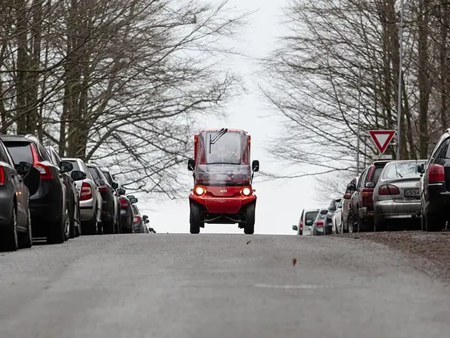 En liten rød elbil fra Posten kjører forbi parkerte biler
