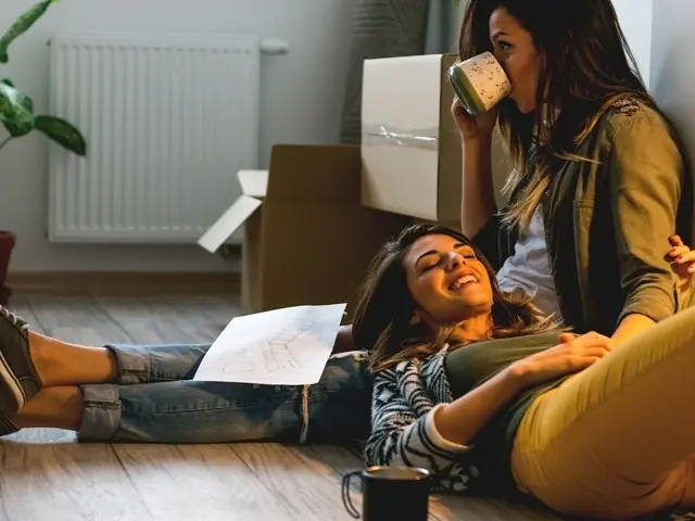 En smilende ung kvinne lener hodet sitt mot fanget til en annen ung kvinne som drikker te