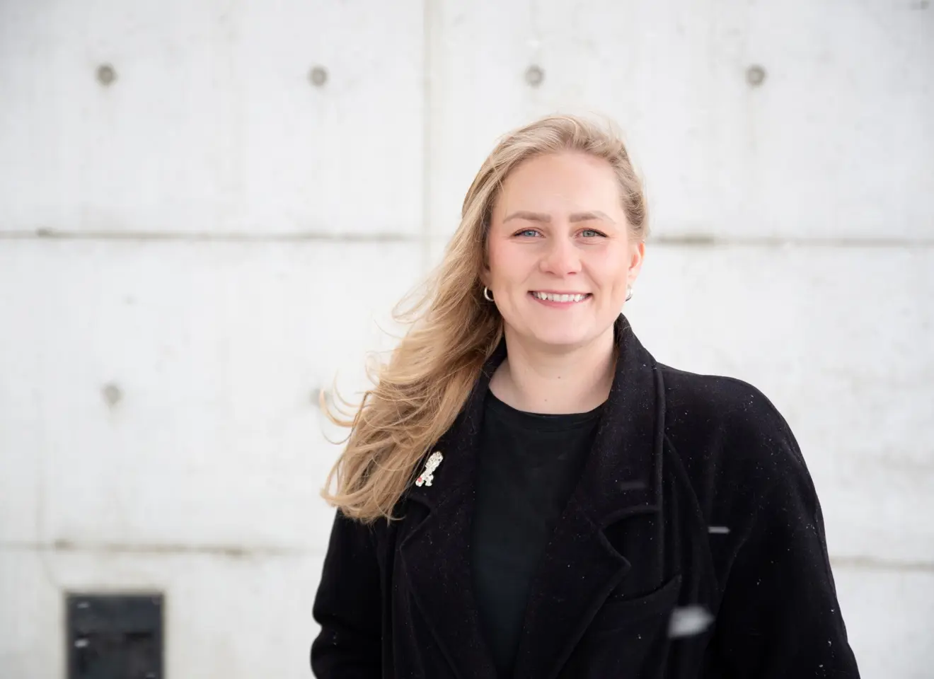 Portrett kvinne med langt lyst hår mot betongvegg