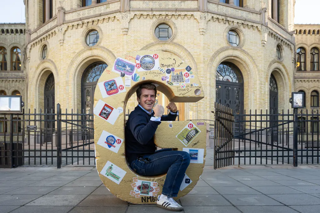 Studentleder Tim sitter inne i en stor G i gull foran Stortinget, jubler med armene