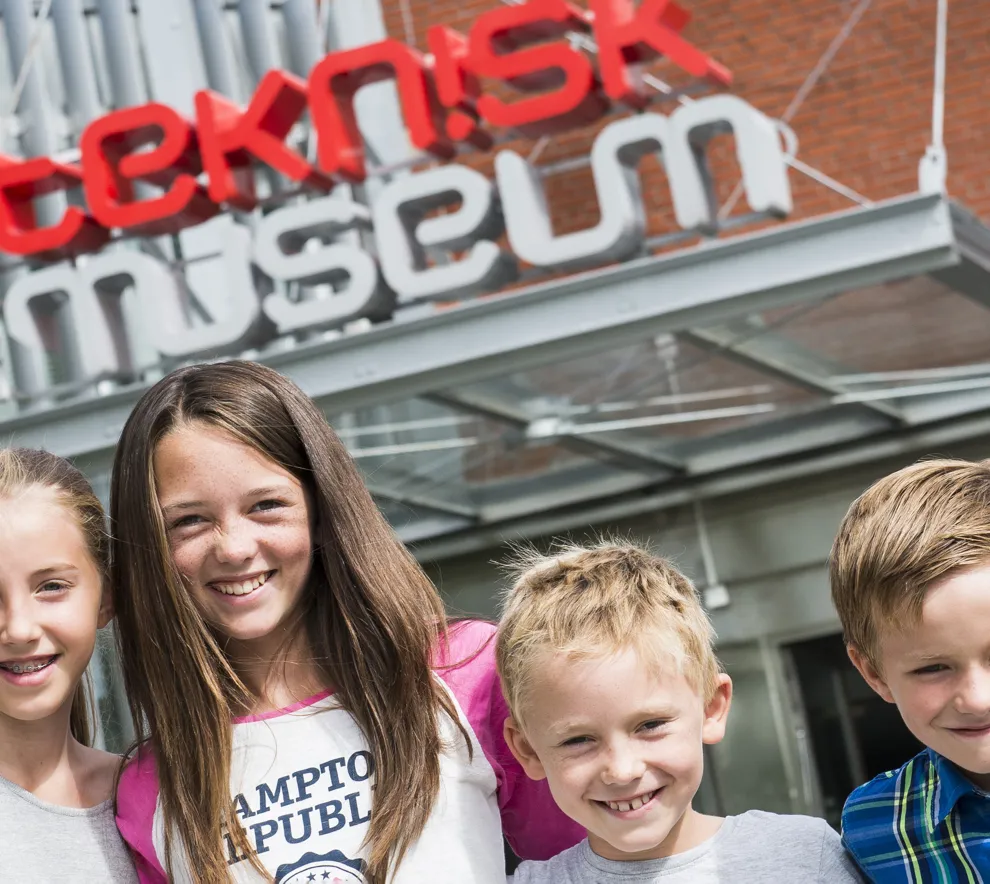 Smilende barn foran hovedinngangen til Teknisk museum i Oslo. 