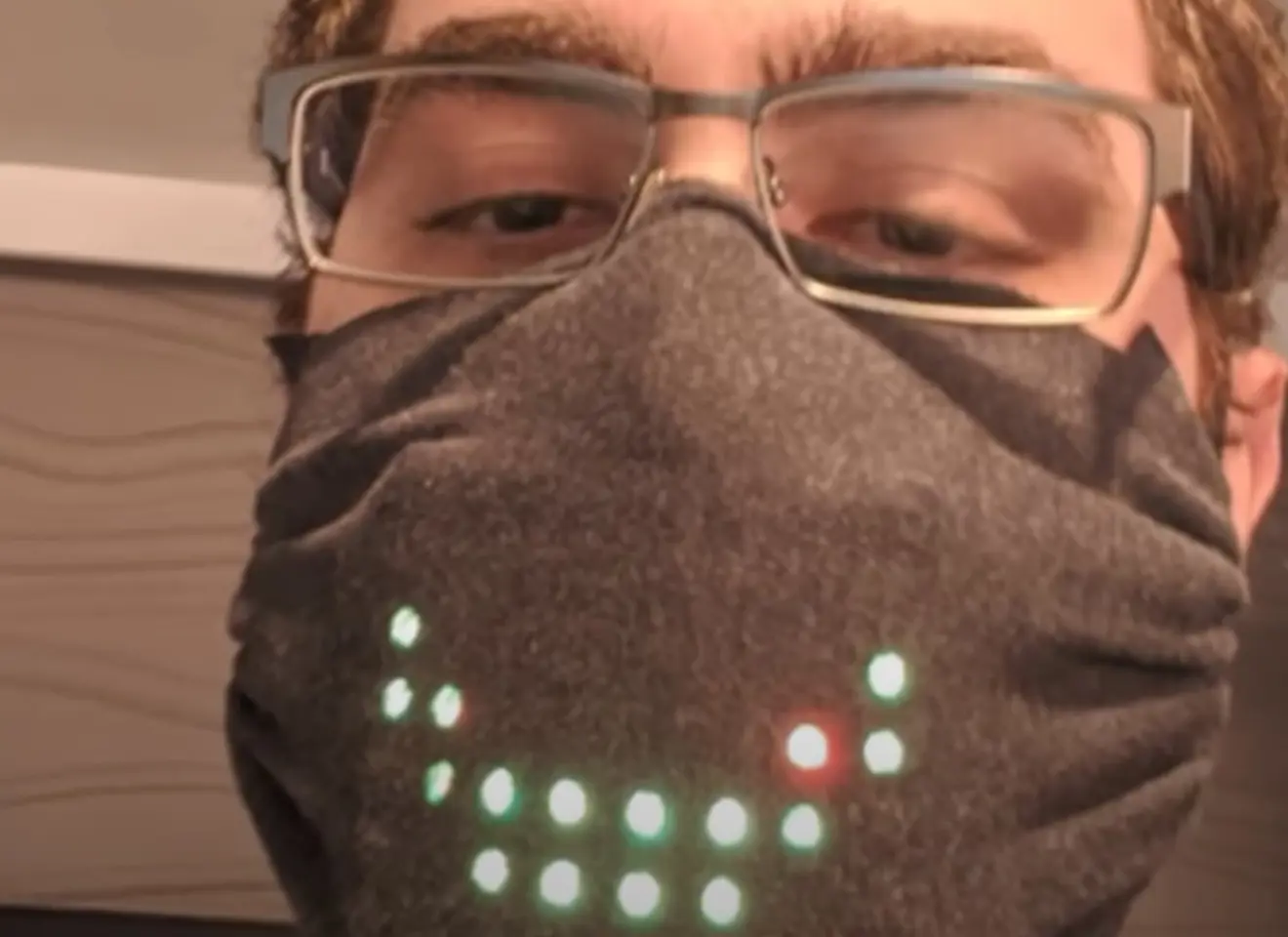 Nærbilde av en mann med briller og COVID maske som har innebygde LED lys som kan styres til å viser f.eks. smilefjes