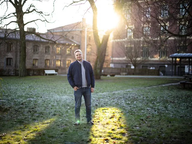 Håvard Solheim står foran et tre i en liten park foran noen byggninger