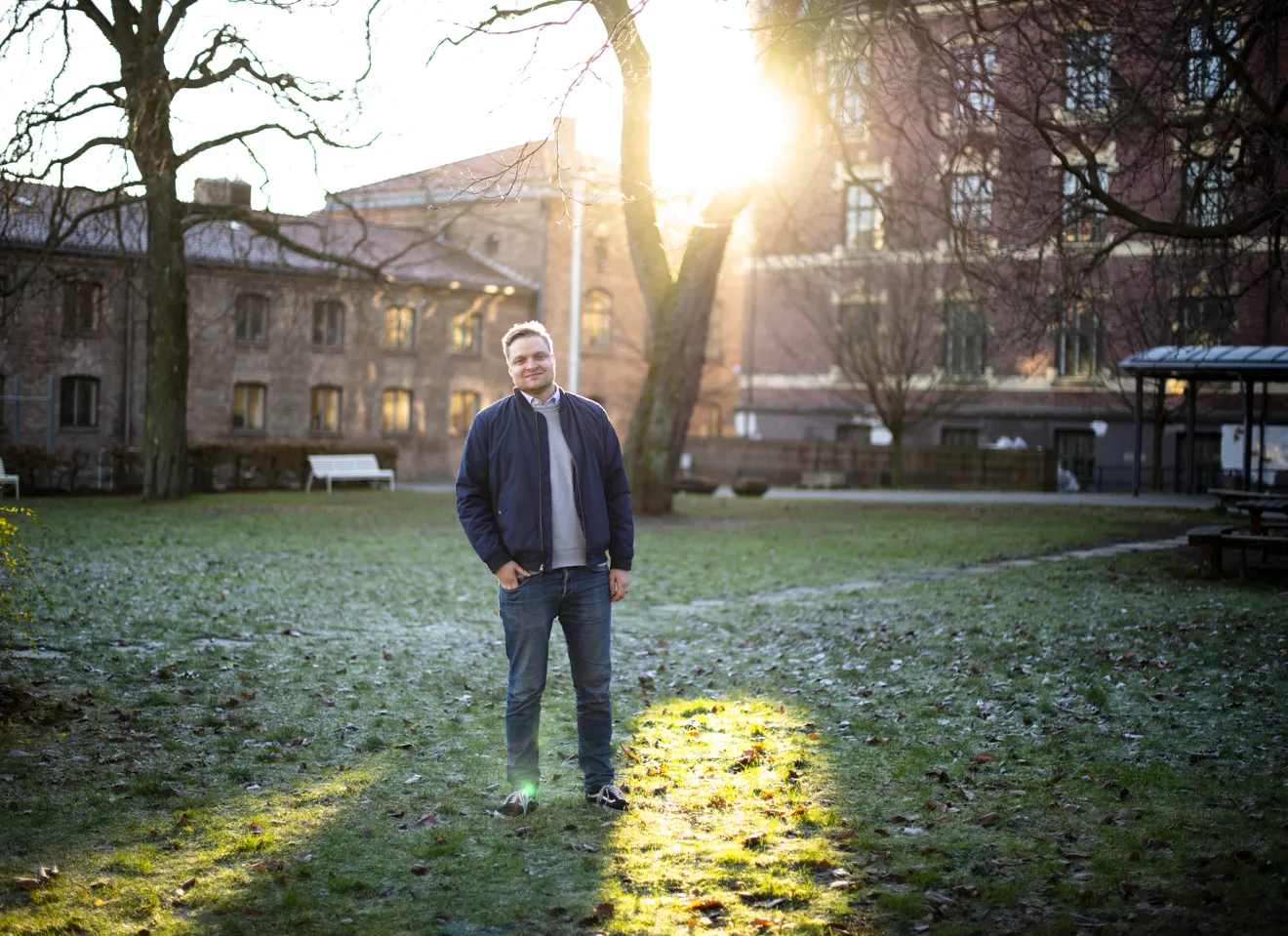 Håvard Solheim står foran et tre i en liten park foran noen byggninger